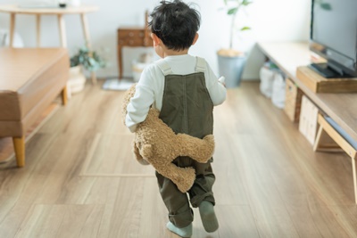 秋の昼間の家の中でくまのぬいぐるみを抱えて走る日本人の子供の後ろ姿